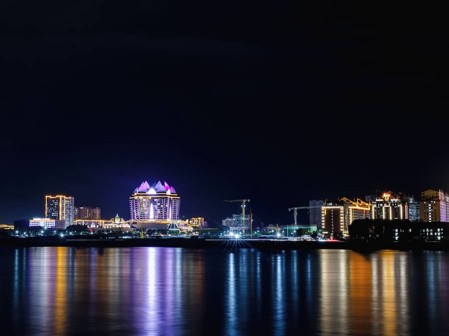 A nighttime cityscape with illuminated buildings reflecting on the water.