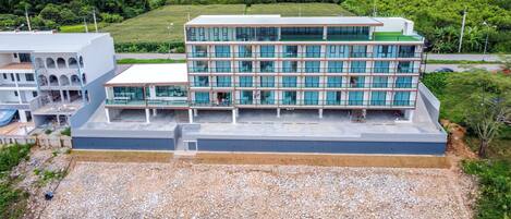 A modern multi-story building with a flat roof and large windows, situated near a riverbank with a rocky embankment.