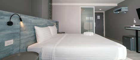 A modern hotel room with a large bed, bedside table, and a desk with a chair.