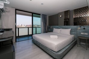 Una habitación de hotel moderna con una cama grande, un escritorio y vistas de la ciudad a través de un ventanal amplio.