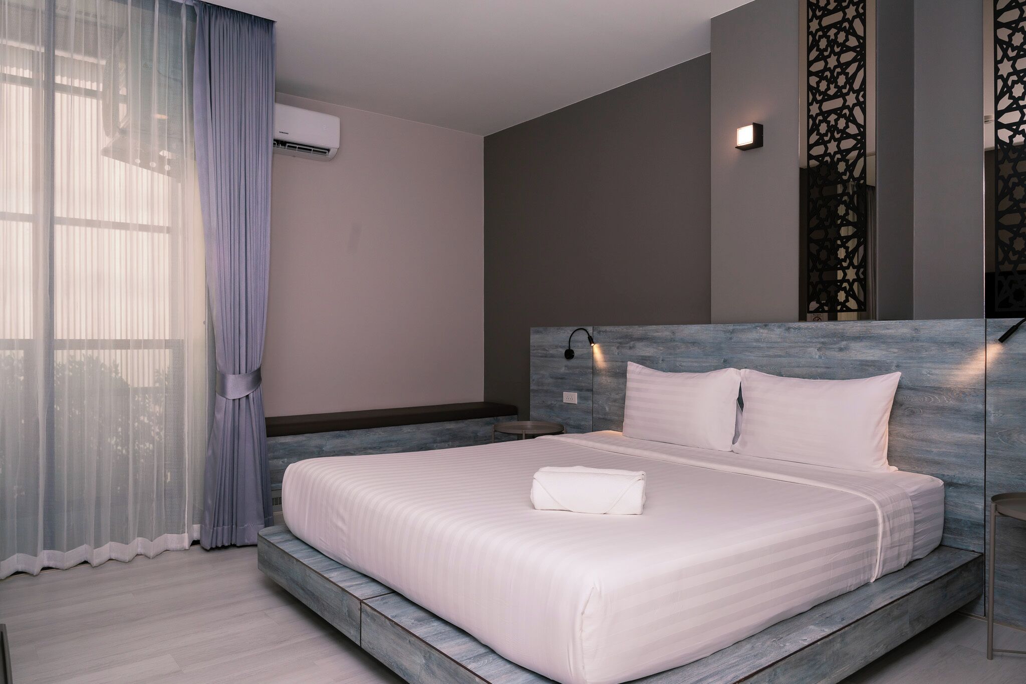 Una habitación de hotel moderna con una cama grande, cabecera con iluminación integrada, aire acondicionado montado en la pared y un panel decorativo.