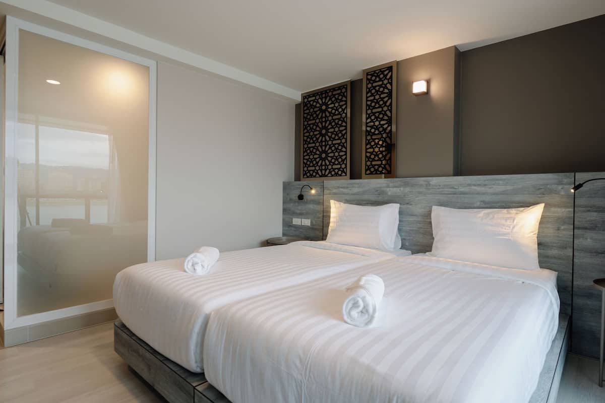 A double bed with white linens and two pillows, a nightstand with a lamp, and a decorative wall panel.