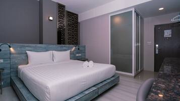 A modern hotel room with a large bed, a seating area, and a sliding glass door leading to a balcony.