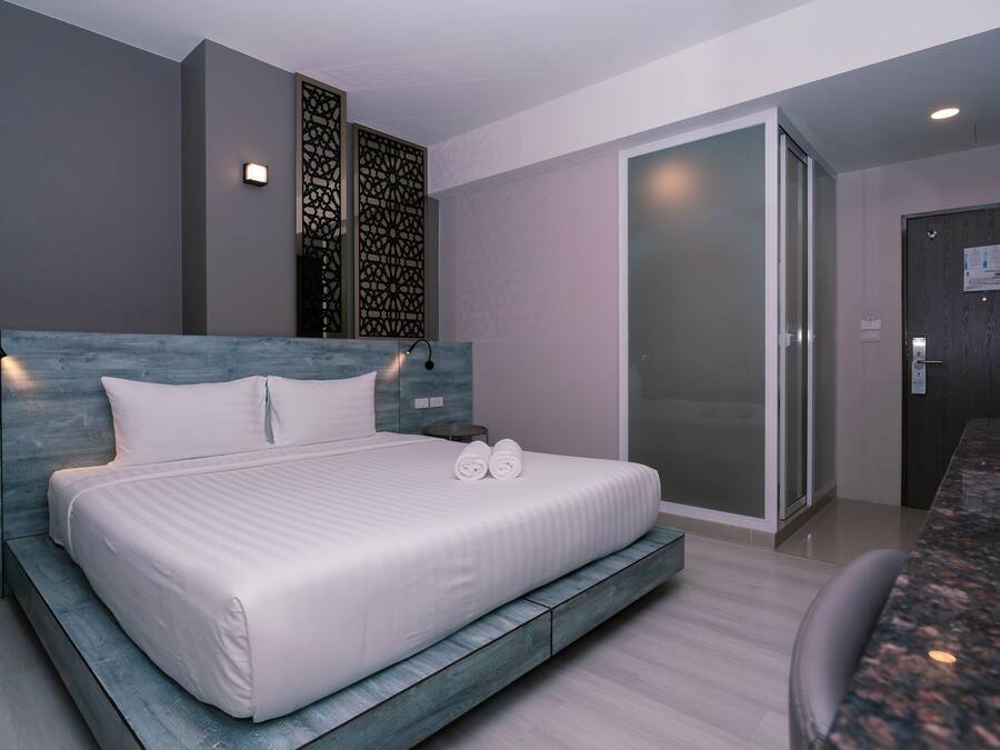 A modern hotel room with a large bed, a seating area, and a sliding glass door leading to a balcony.