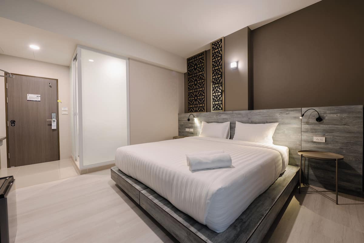 A modern hotel room with a large bed, a wooden headboard, a small bedside table, and a decorative wall panel.