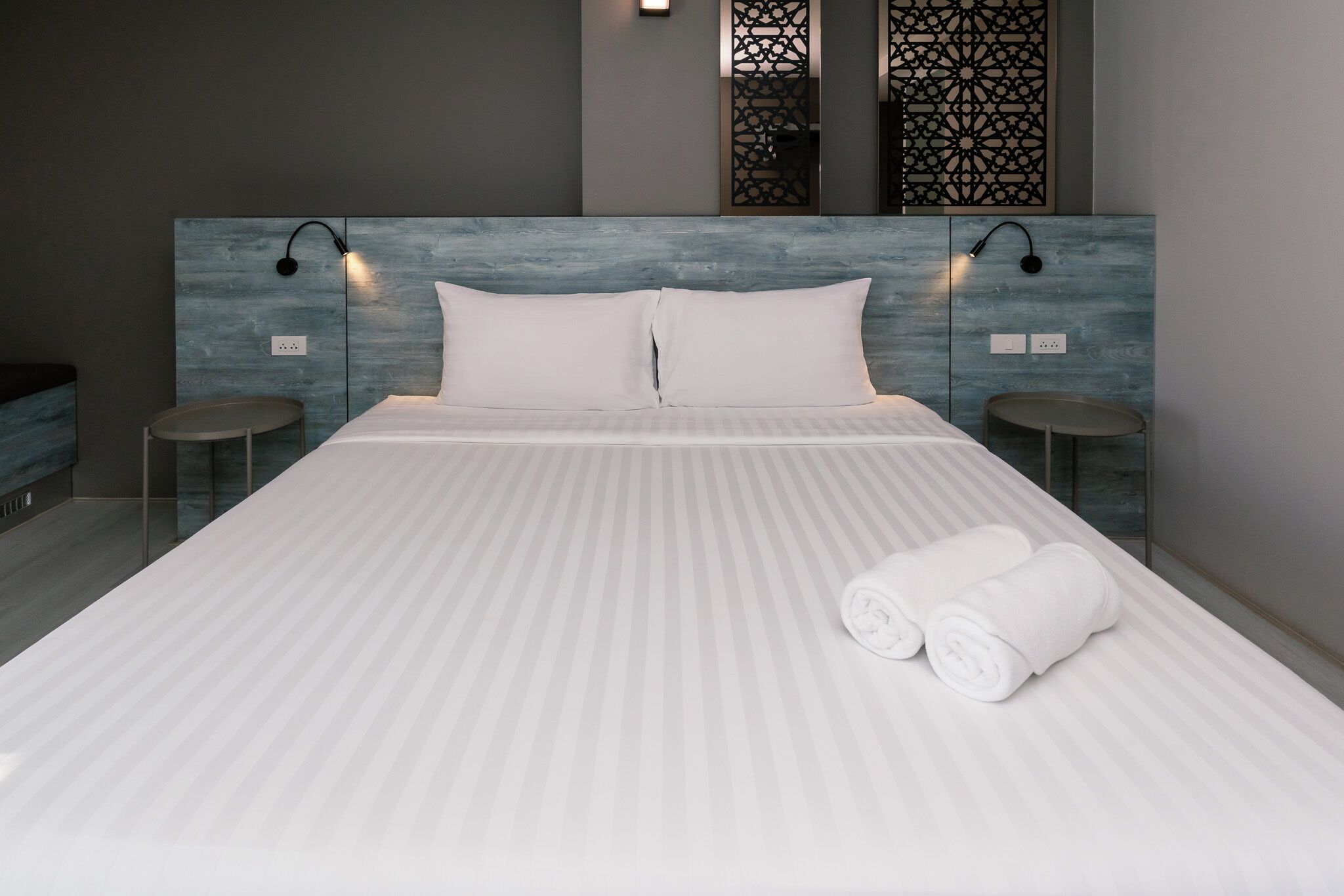 A modern hotel room with a large bed, two bedside tables, and a headboard with integrated lighting.
