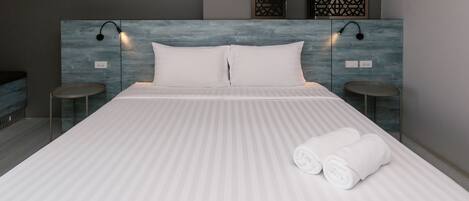A modern hotel room with a large bed, two bedside tables, and a headboard with integrated lighting.
