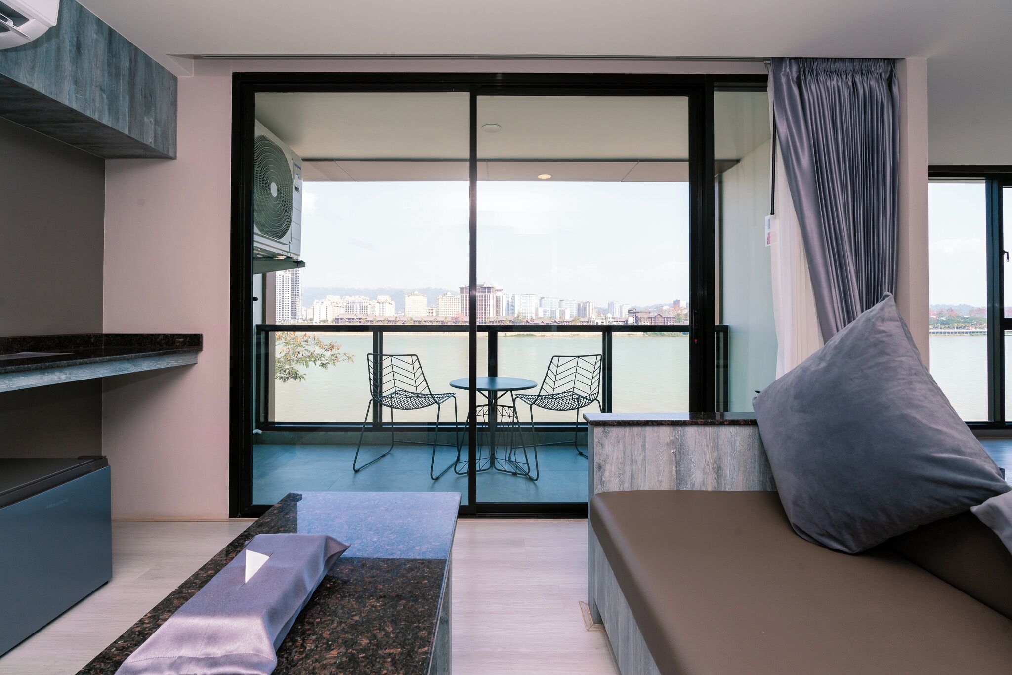 A modern living room with a sofa, a small table, and two chairs. A large window offers a view of a cityscape.