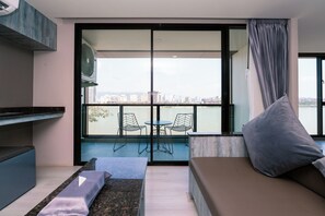Una sala de estar moderna con un sofá, una mesita y dos sillones. Un ventanal grande ofrece vistas a un paisaje urbano.