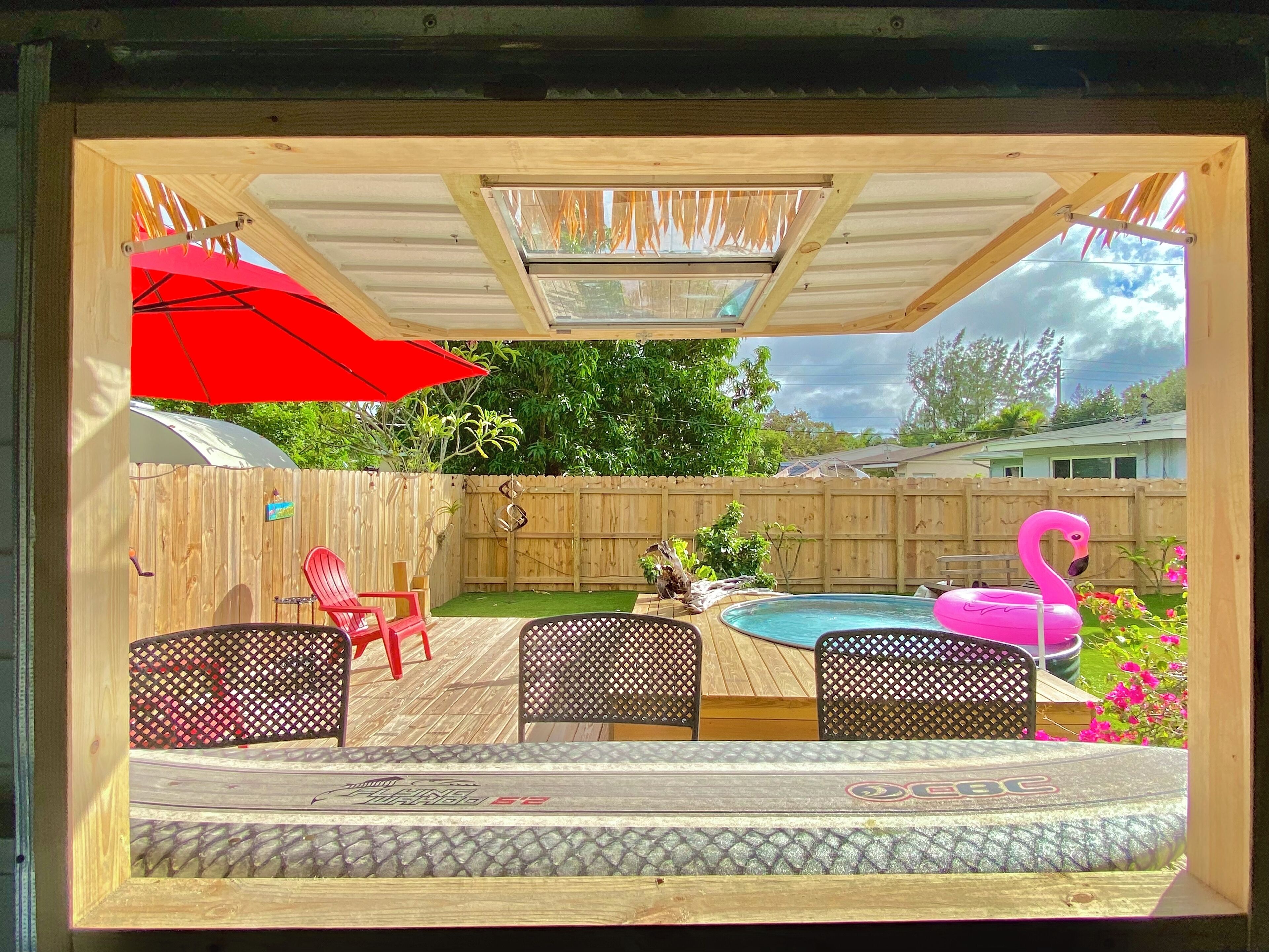 Een achtertuin met een houten terras, een zwembad en een flamingo drijver.