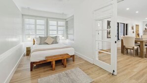 A bedroom with a wooden bed, a window with blinds, a bedside table, and a view into a dining area. - Charming Farmhouse style w/cowboy pool in Fort Lauderdale (Fort Lauderdale)