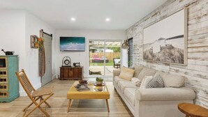 A living room with a sofa, coffee table, and a wooden chair. There is a painting on the wall and a window with a view of the outdoors. - Charming Farmhouse style w/cowboy pool in Fort Lauderdale (Fort Lauderdale)