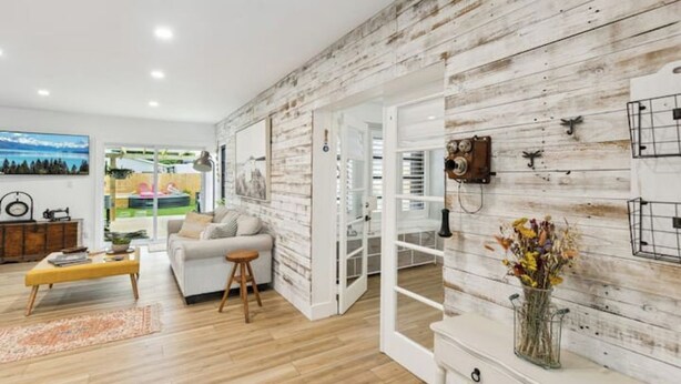 A modern living room with a wooden wall, a sofa, a coffee table, and a vase with flowers. - Charming Farmhouse style w/cowboy pool in Fort Lauderdale (Fort Lauderdale)