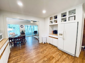 A spacious kitchen with wooden flooring, white cabinetry, and a built-in refrigerator.