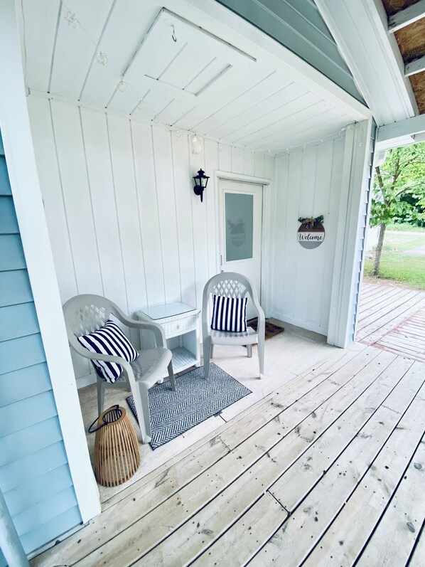 A porch with two white chairs, a small table, and a welcome sign.