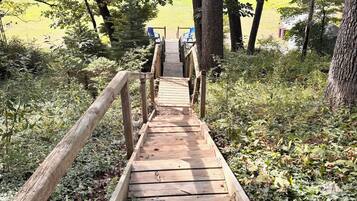 A wooden pathway leading to a seating area with chairs, surrounded by trees and greenery.