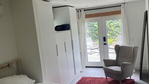 Une chambre à coucher comprenant un lit, une armoire, une chaise et une porte-fenêtre coulissante donnant sur un espace extérieur.