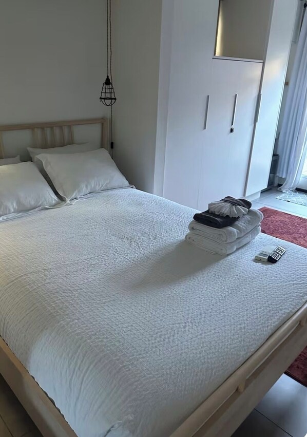 A neatly made bed with white linens, a hanging light fixture, and a wardrobe with a mirror. - Studio in La Jolla (San Diego)