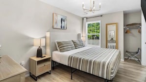 Une chambre à coucher avec un lit, une table de chevet, une lampe, une fenêtre et un lustre.