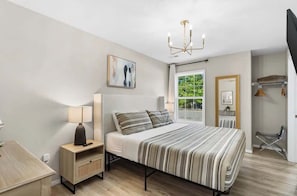 Une chambre à coucher avec un lit, une table de chevet, une lampe, une fenêtre et un lustre.