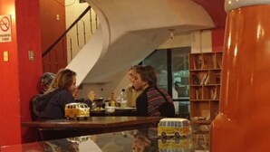 Un espace bar avec un comptoir en verre, une maquette de bus jaune et un escalier en arrière-plan.