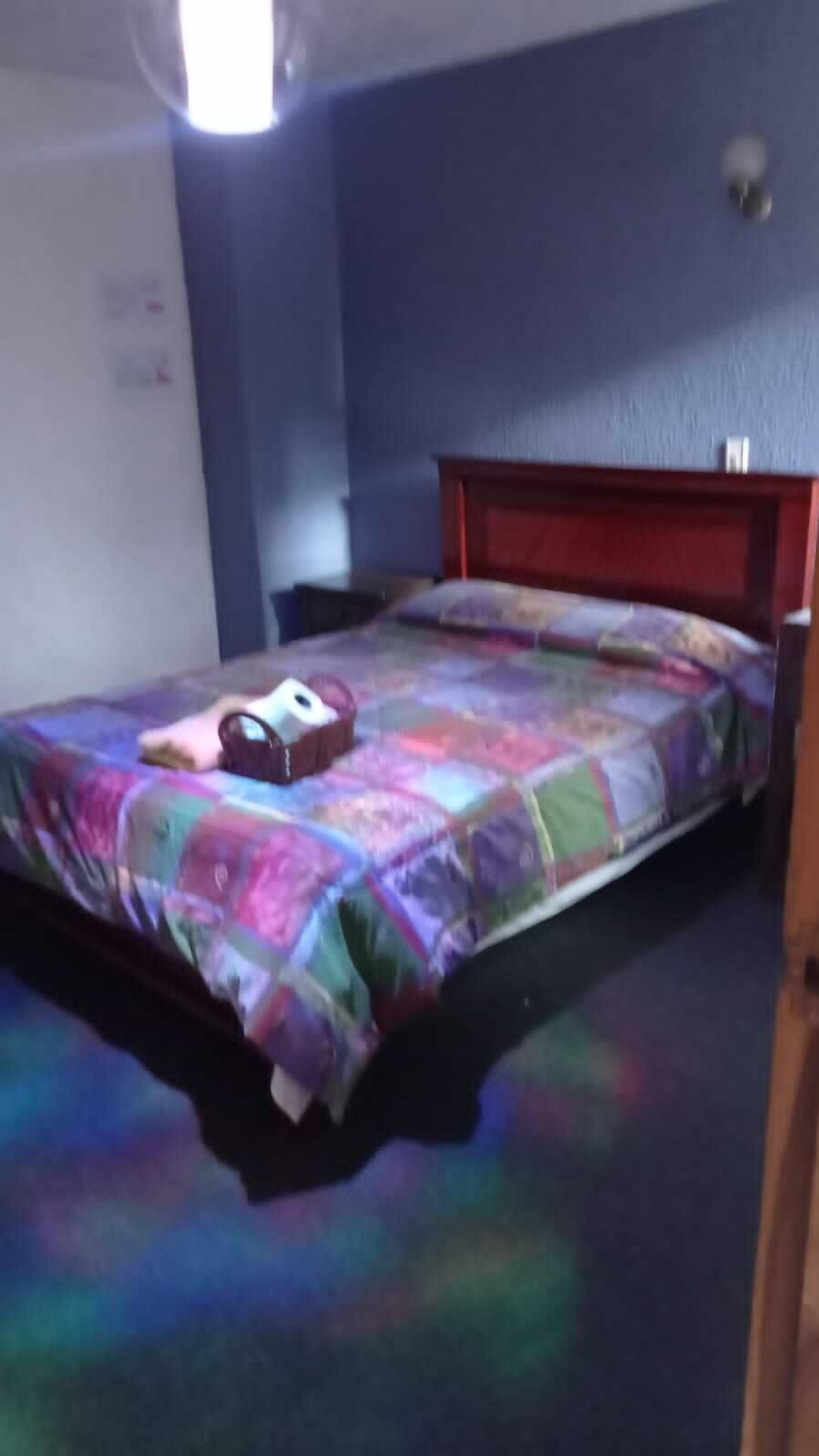 Uma cama de solteiro com um edredom colorido, uma cabeceira de madeira e uma mesa de cabeceira com um abajur.