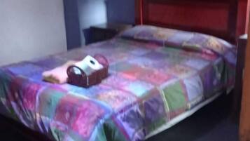 Uma cama de solteiro com um edredom colorido, uma cabeceira de madeira e uma mesa de cabeceira com um abajur.