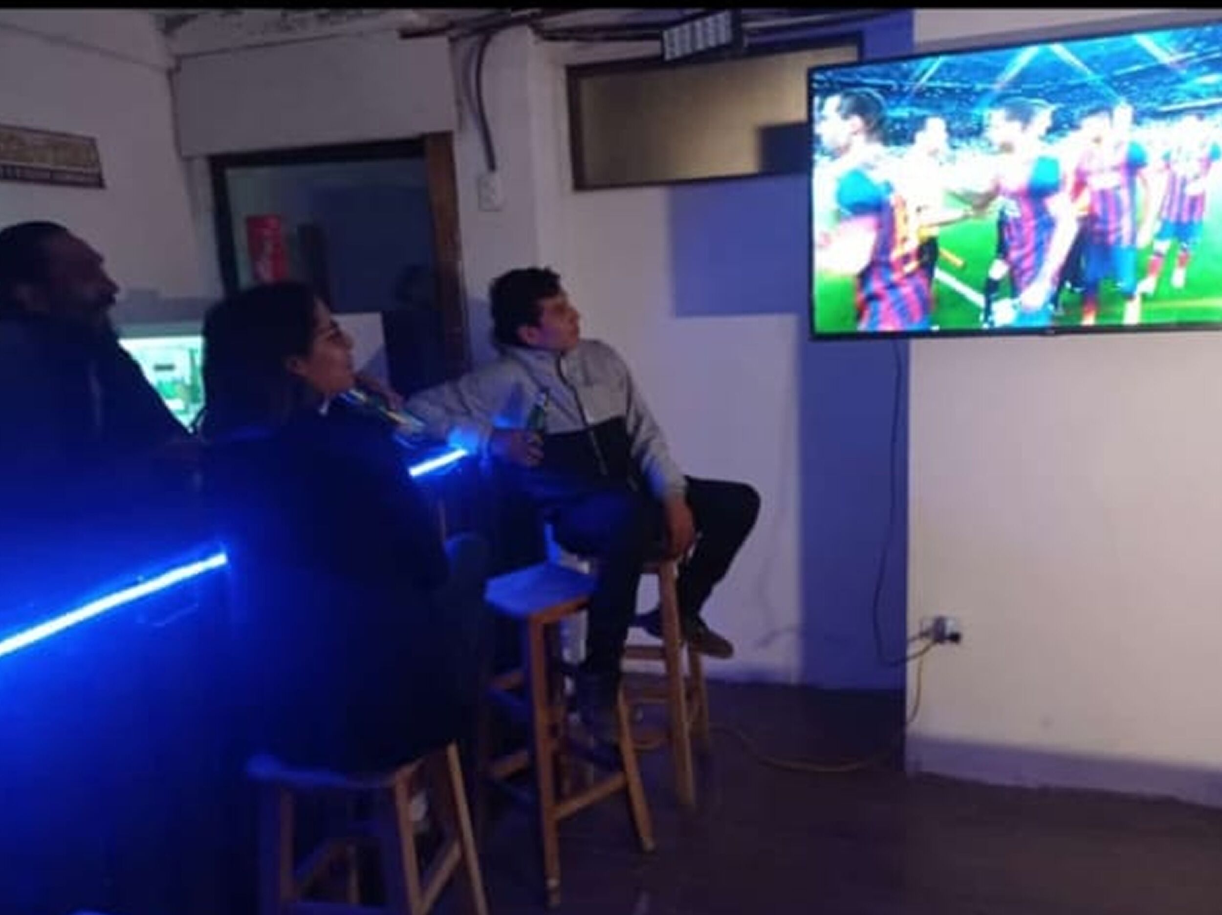 Habitación con una televisión mostrando un evento deportivo, una silla de madera y un estante fijado a la pared.
