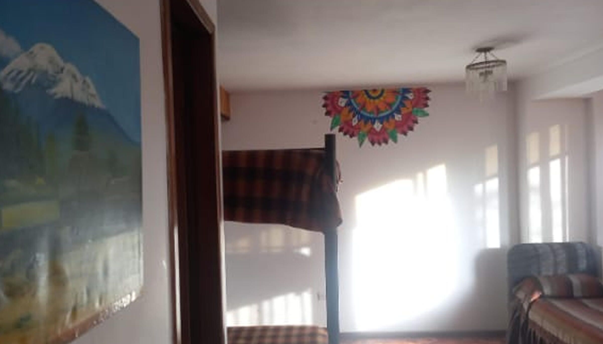 Una habitación con una pintura de montaña, un tapiz de colores, una manta escocesa y un sofá.