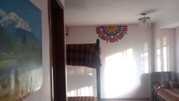 Una habitación con una pintura de montaña, un tapiz de colores, una manta escocesa y un sofá.