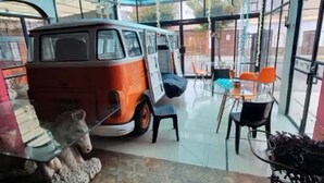 Un restaurant doté d’une terrasse fermée par des baies vitrées, d’un vieux camionnette orange et blanc et d’une statue d’ours.