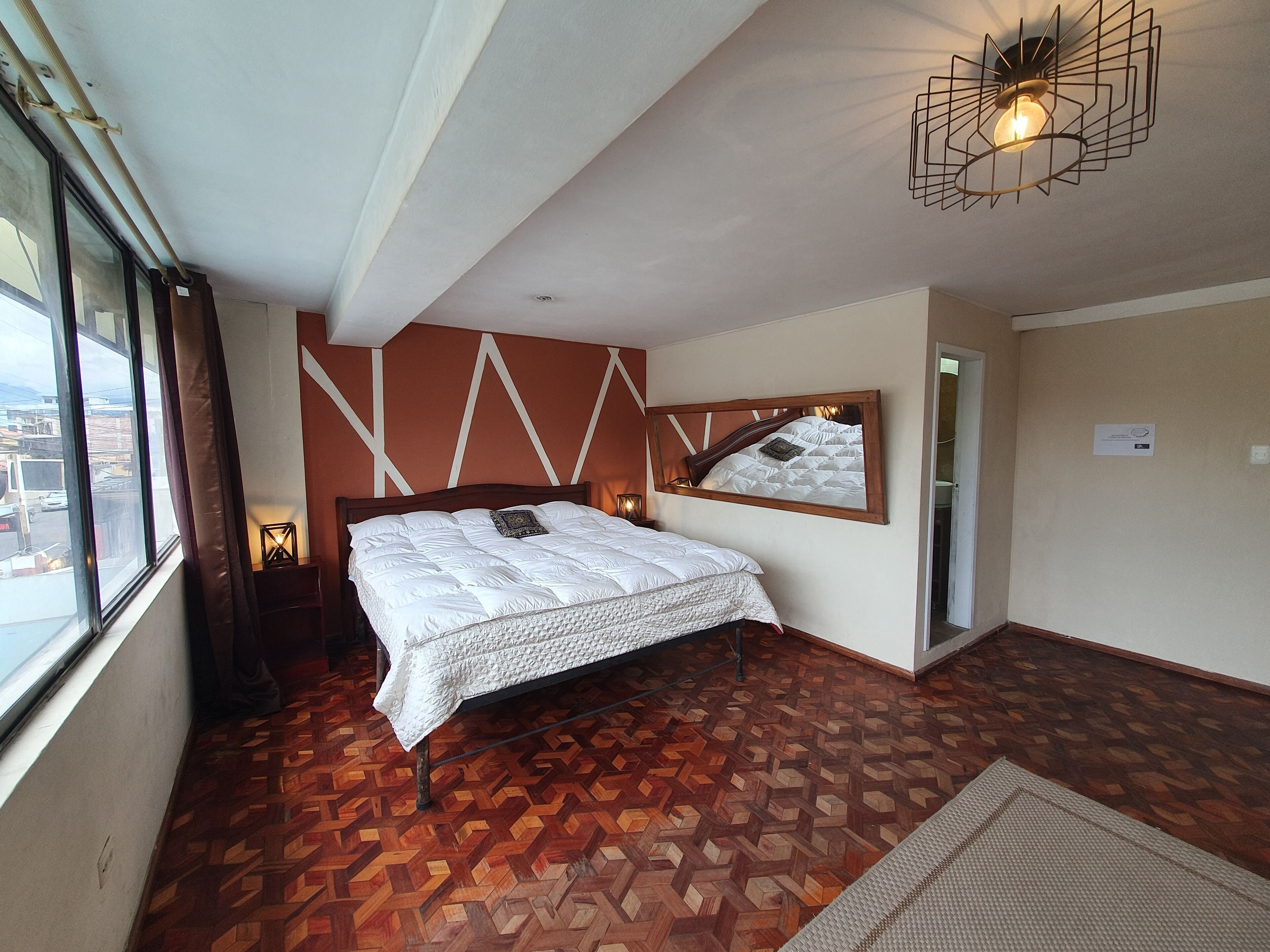Un dormitorio con cama, espejo y vistas al exterior a través de una ventana.