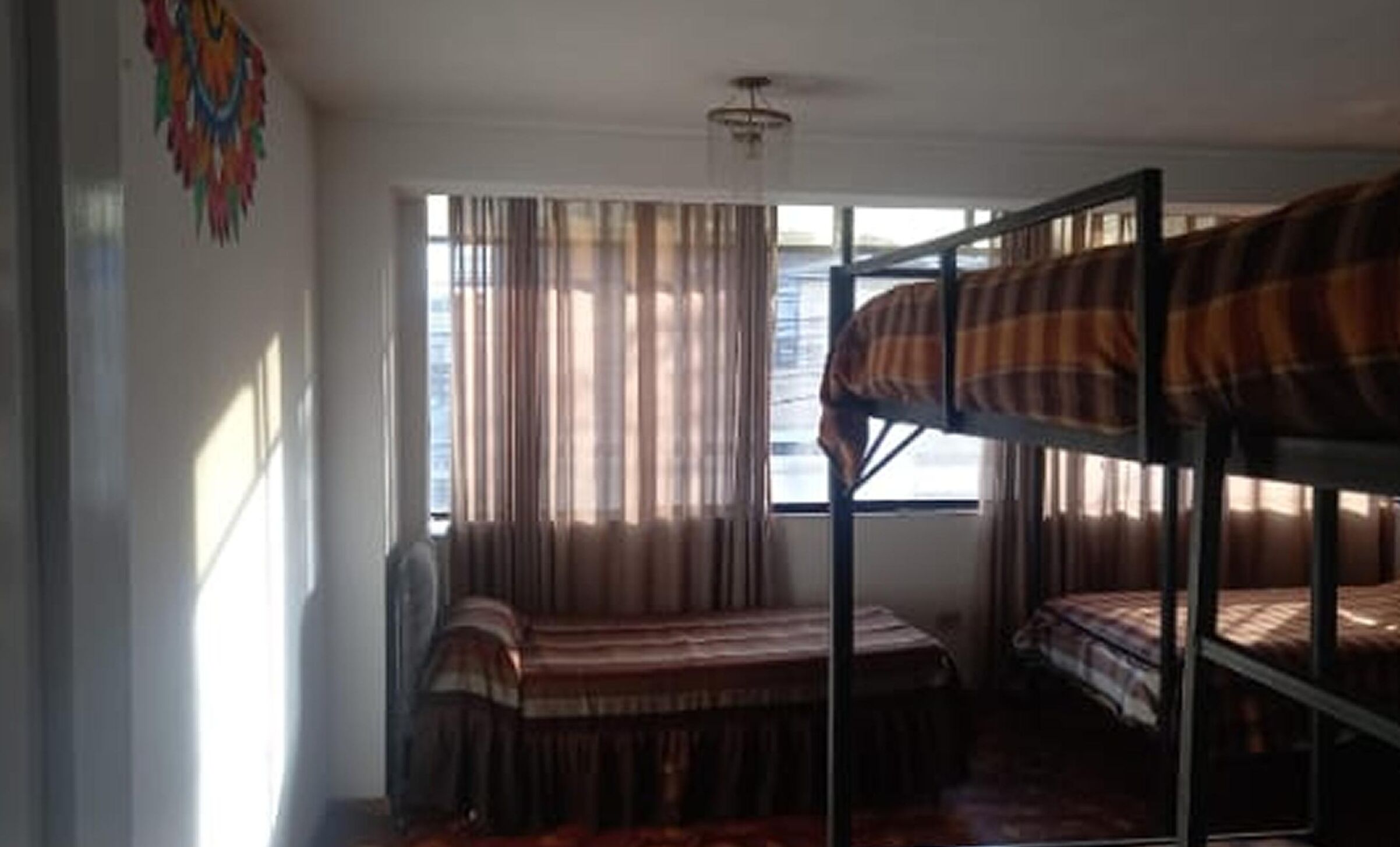 A dormitory room with bunk beds, a window with curtains, and a ceiling fan.