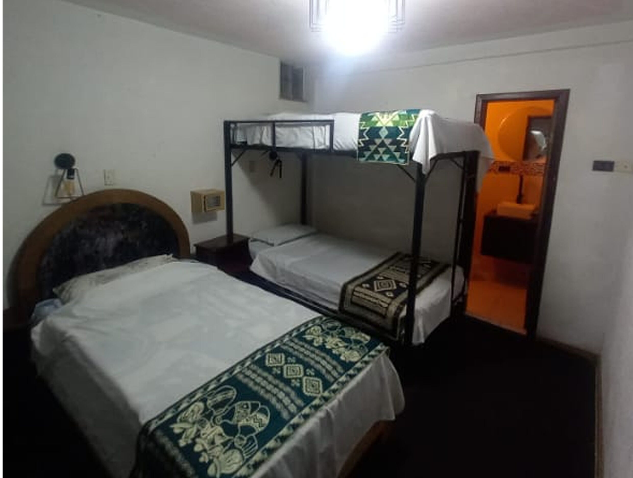 Una habitación con dos literas, un cabecero de madera, una mesita de noche y una ventana pequeña.