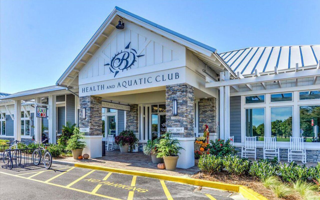 The exterior of a health and aquatic club with a stone facade, a sign indicating it was established in 2017, and outdoor seating.