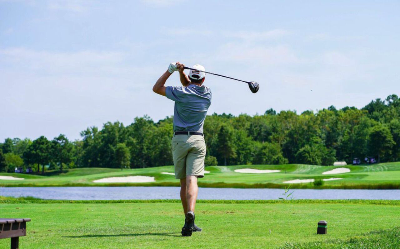 Ein Golfspieler auf einem Golfplatz, im Hintergrund ein See und Bäume.