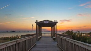 Un muelle de madera que lleva a un pabellón con un emblema circular, con vista a una masa de agua al atardecer.
