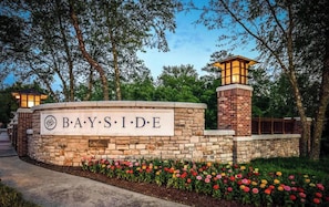 Eine Steinsäule mit dem Schriftzug "BAYSIDE", umgeben von einem angelegten Garten mit bunten Blumen.