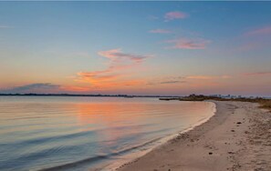 A beach with calm waters reflecting the sunset sky.