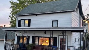 Una casa de dos pisos con un porche cubierto, una chimenea de ladrillo y un ventanal pequeño.
