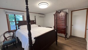 Un dormitorio con una cama con dosel, un aparador de madera, una silla y una ventana con persianas.