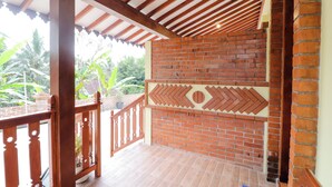 A covered outdoor area with a brick wall, wooden railing, and a view of greenery. - Homestay Nike Bed (Borobudur)