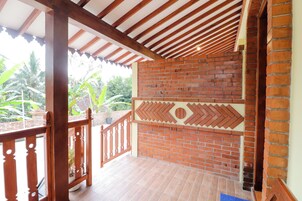 Un espacio al aire libre techado con pared de ladrillo, baranda de madera y vista a la vegetación.