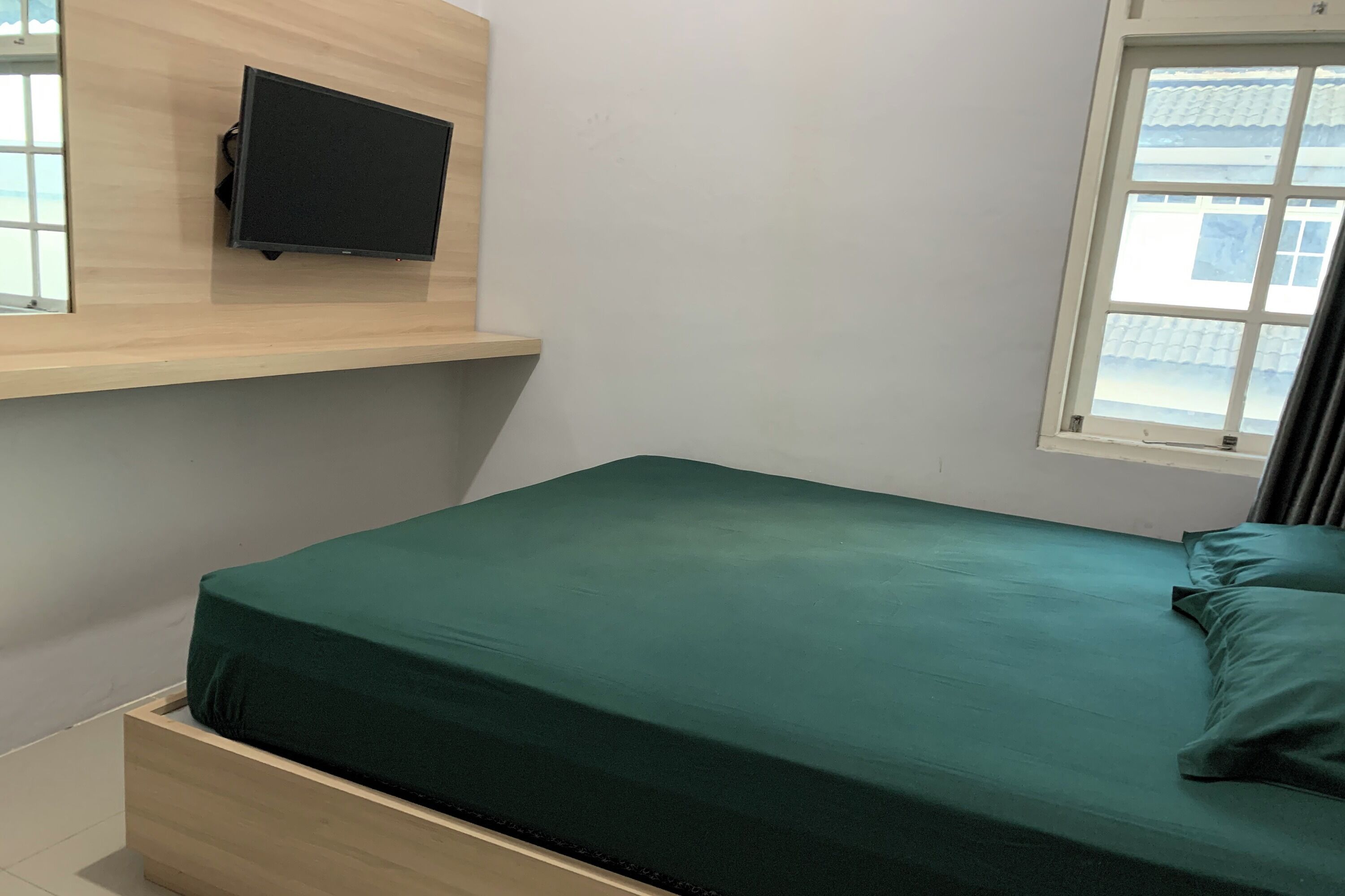 A room with a bed, a mounted TV, and a window with a view of buildings.