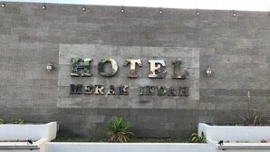 Een hotelschilder met de naam 'HOTEL MERAK INDAH' op een structuurmuur.