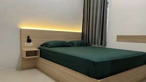 Een moderne slaapkamer met een houten bedframe, groen beddengoed, een nachtkastje met lamp en uitzicht op de lucht door gordijnen.