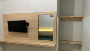 Een kamer met een aan een houten wand bevestigde televisie, een rookverbodsgevaarsbord en uitzicht op een ondergaande zon door een raam.
