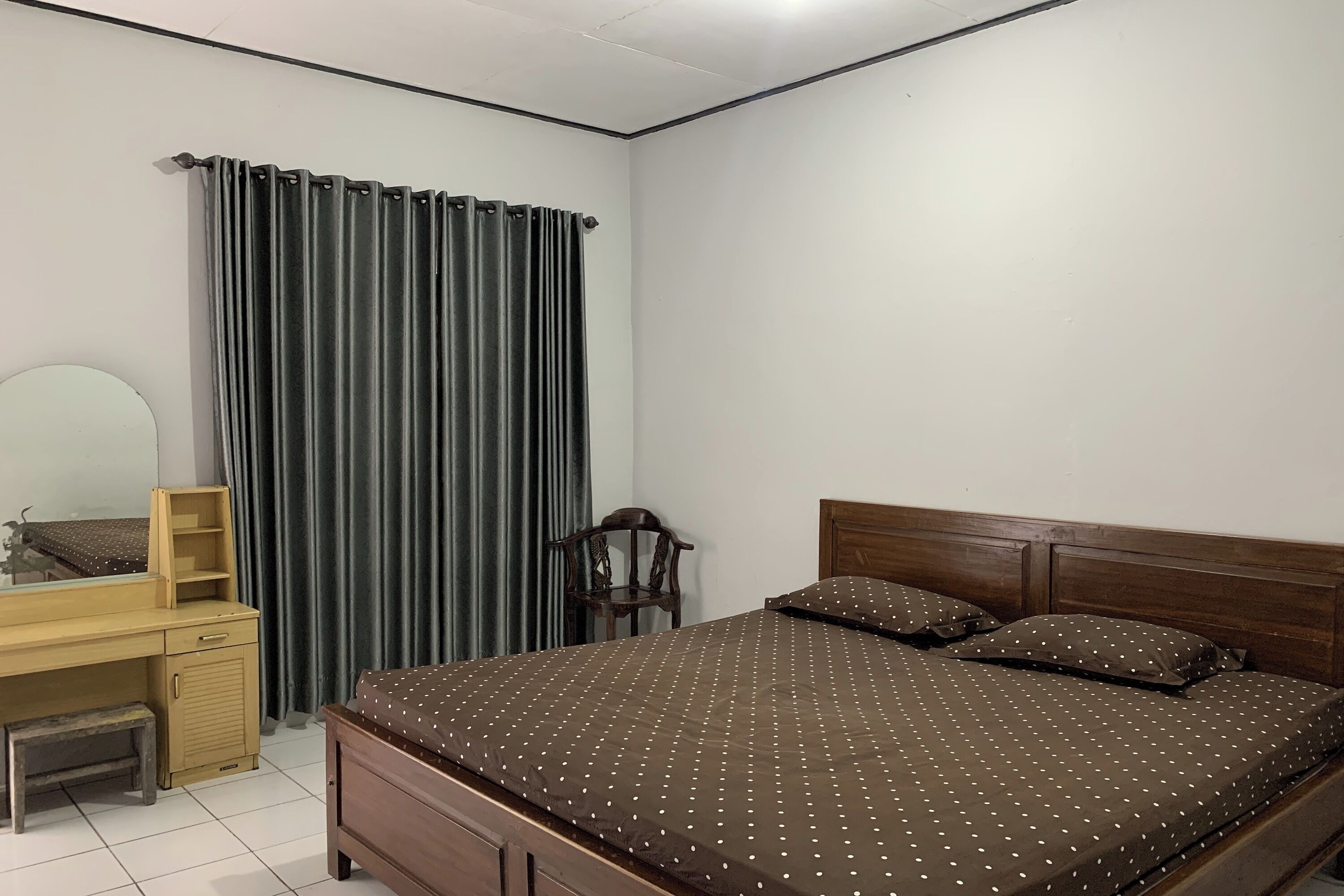 Quarto com uma cama, escrivaninha de madeira, cadeira e espelho.