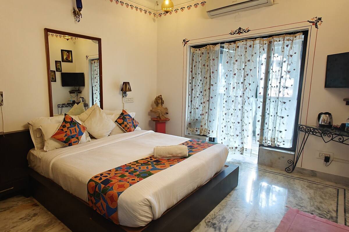 A well-lit bedroom with a large bed, a television, and a window with floral curtains.