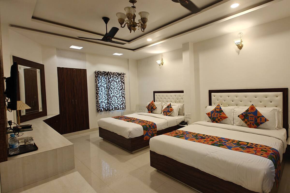 A hotel room with two beds, a sitting area, a wardrobe, a mirror, and a chandelier.